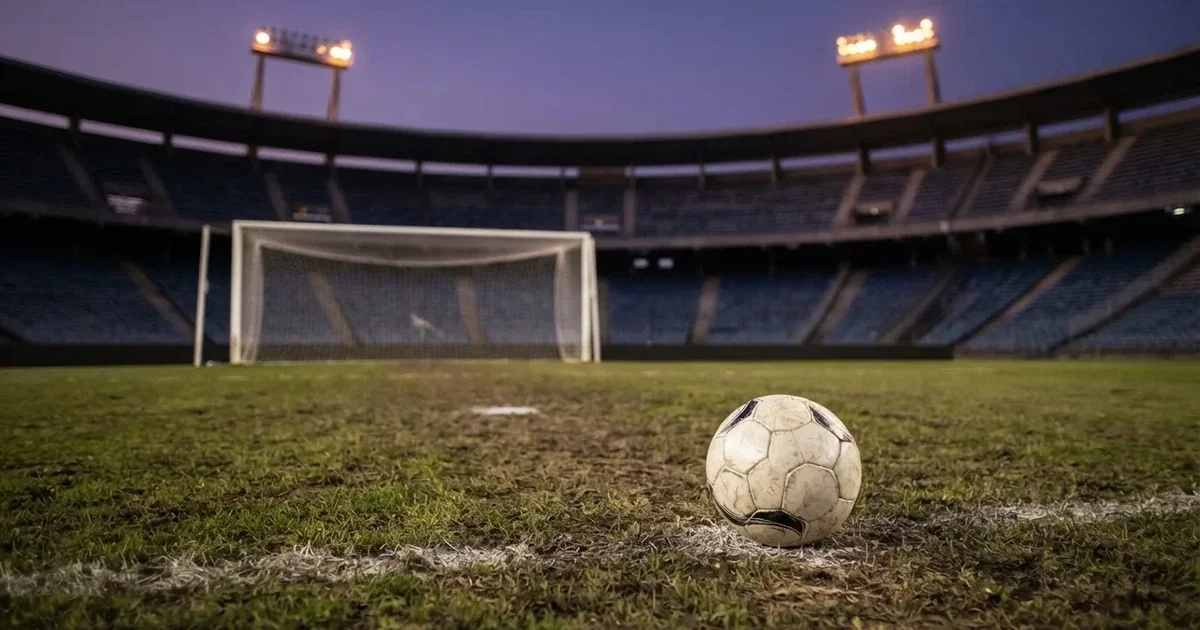 Ein Fußball liegt im Strafraum direkt vor dem Tor mit Netz, im Hintergrund leere Ränge bei Dämmerung.